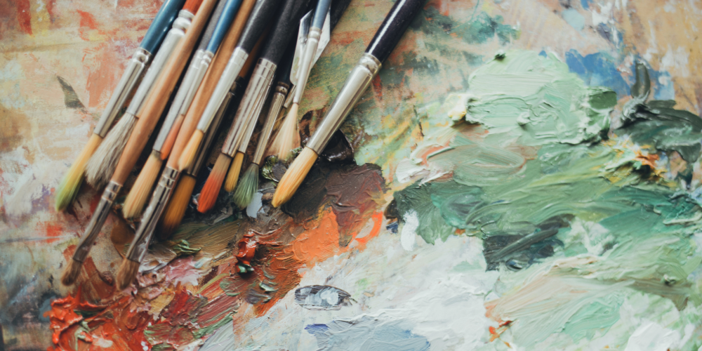 Stock image of multiple colored and sized paint brushes with different color paints mixing