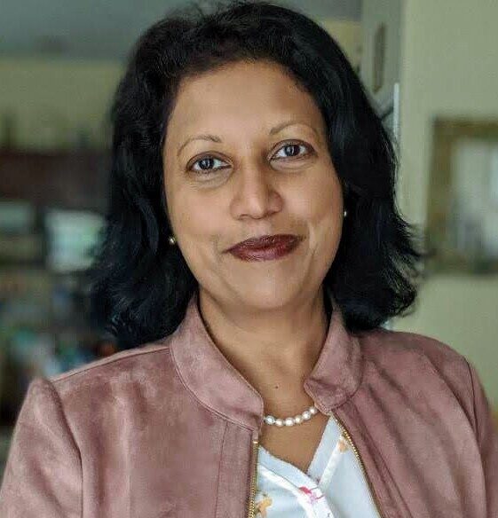 Professional headshot of Manjari Wijenaike wearing a light jacket and pearl necklace, photographed indoors with a softly blurred background.