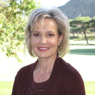 Head-and-shoulders outdoor portrait of Rebecca Eddy wearing a dark burgundy sweater, with trees and mountains in the background