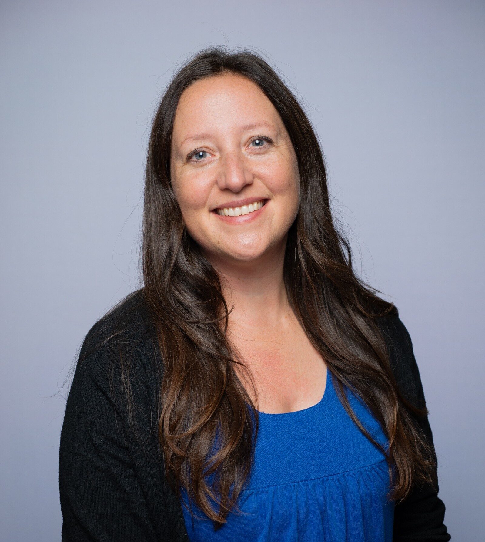 Professional portrait of Sara Guenther wearing a blue top and black cardigan, photographed against a light gray background.