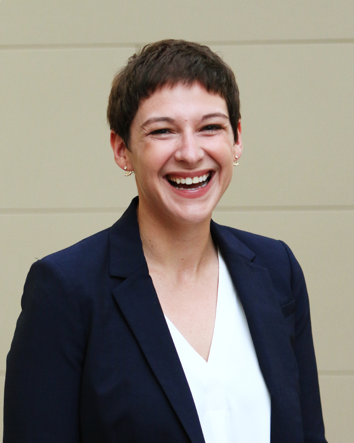 Professional portrait of Megan William in a navy blazer and white shirt against a neutral indoor background.
